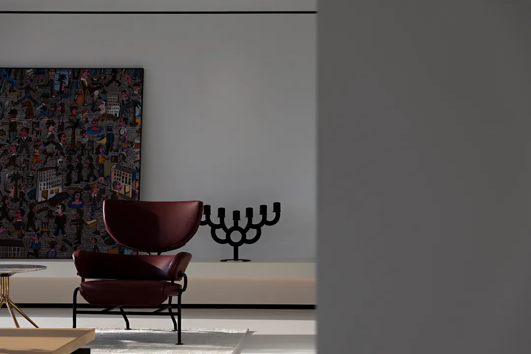 A modern living room featuring a leather armchair, a large abstract artwork, and a black candlestick holder.
