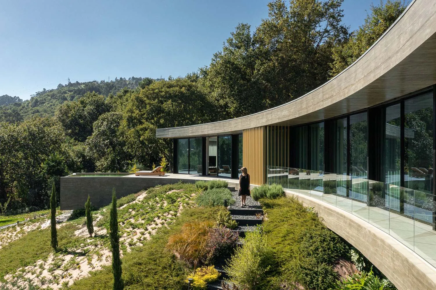 A modern wooden and stone-clad house nestled in a forested area with a panoramic view.