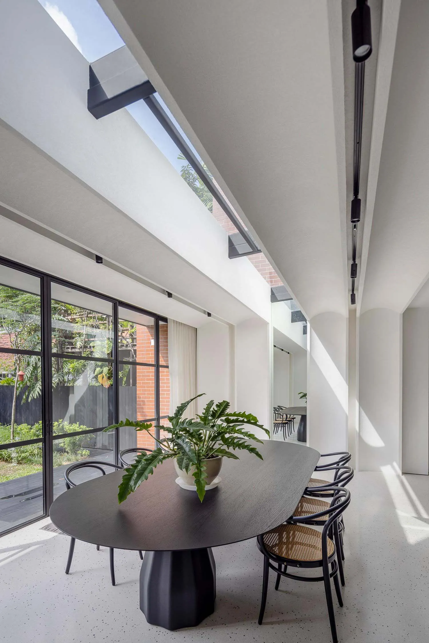 A modern minimalist dining room featuring a sleek black table with a geometric base, surrounded by black chairs with cane bac