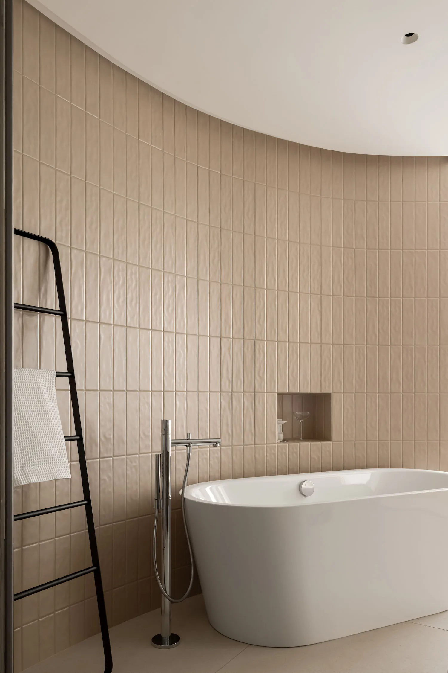 A minimalist bathroom with tiles and a concrete bathtub, featuring a black ladder and a recessed shelf.