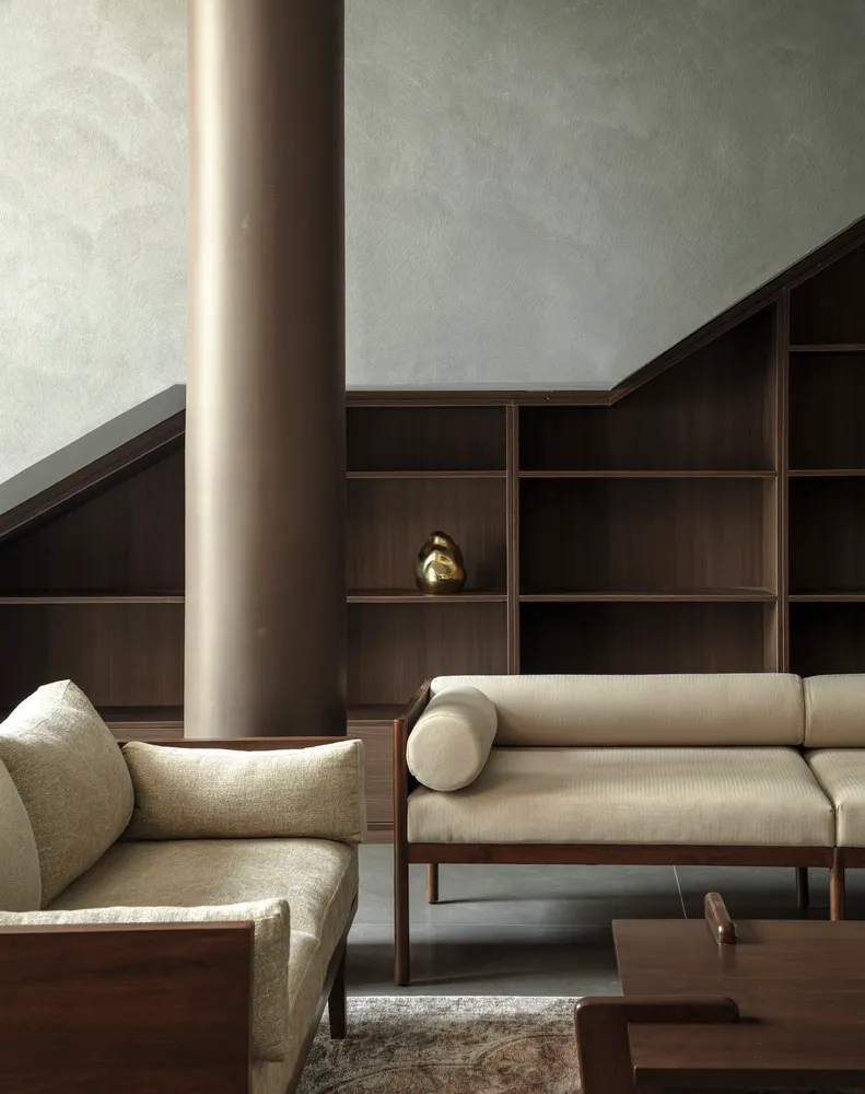A modern living room with a textured wooden column, upholstered fabric seating, and dark wood shelves against a textured wall