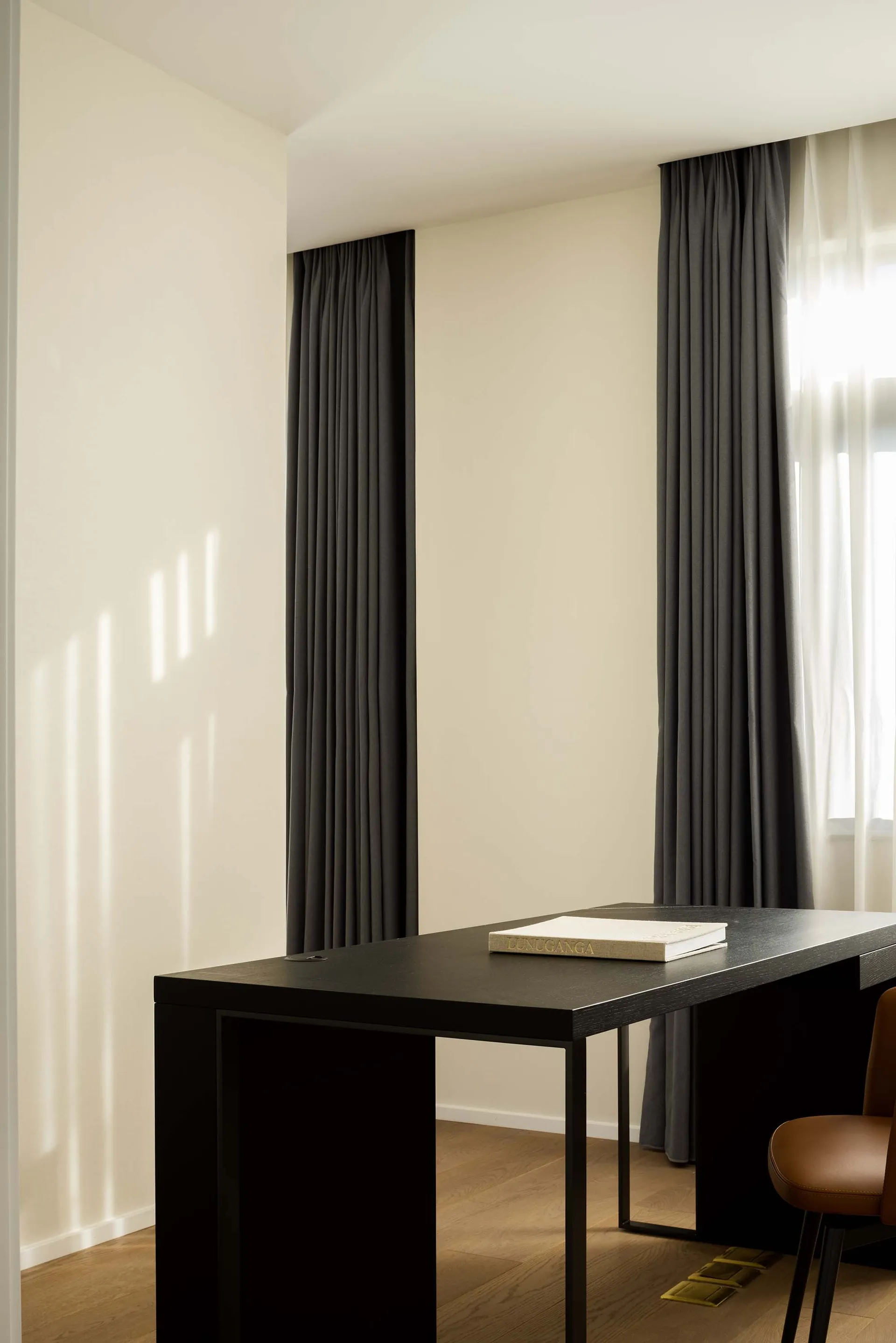 A minimalist interior space featuring gray textured curtains and a wooden floor with sunlight streaming through the windows.
