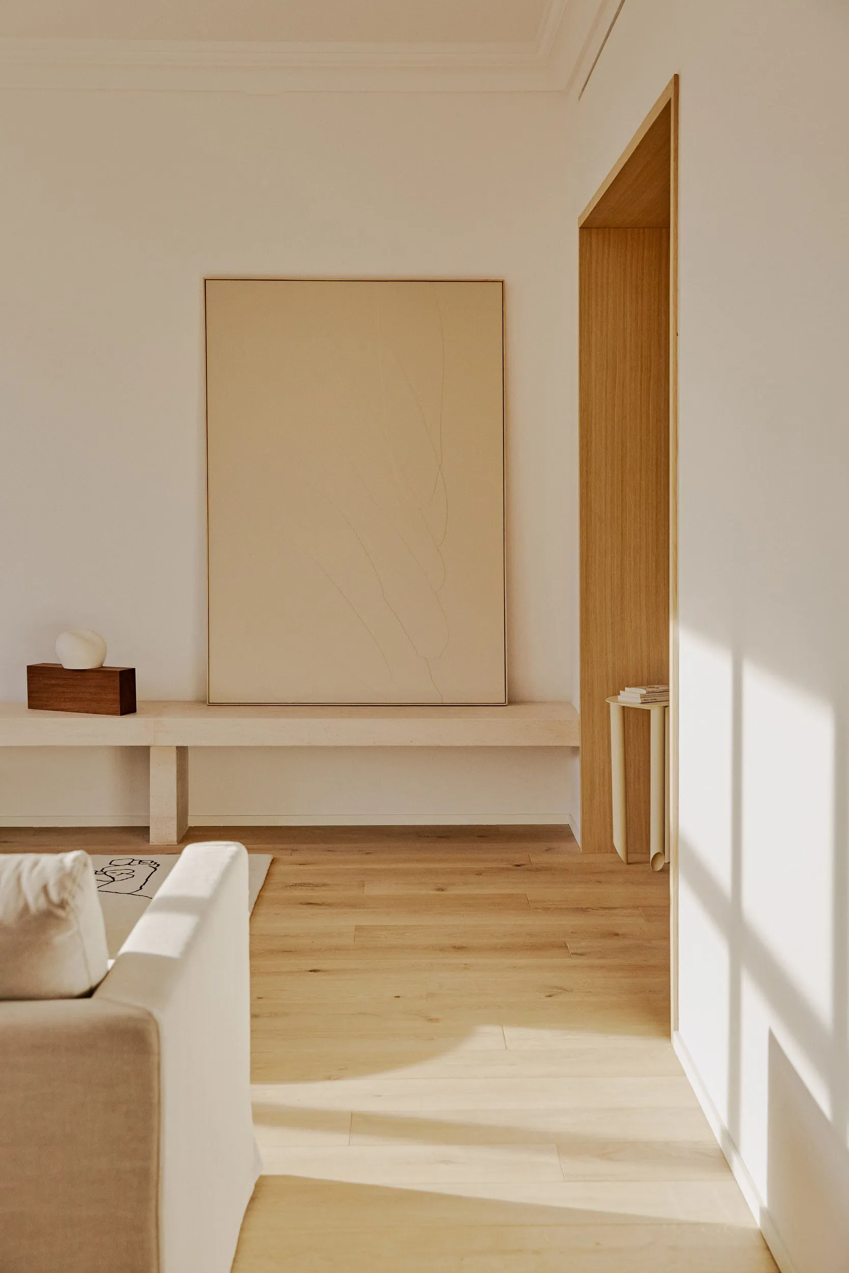 A minimalist living room with natural wood furniture and a large abstract painting.