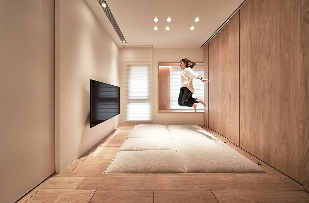 A minimalist residential interior with wooden flooring and light-colored cushions.