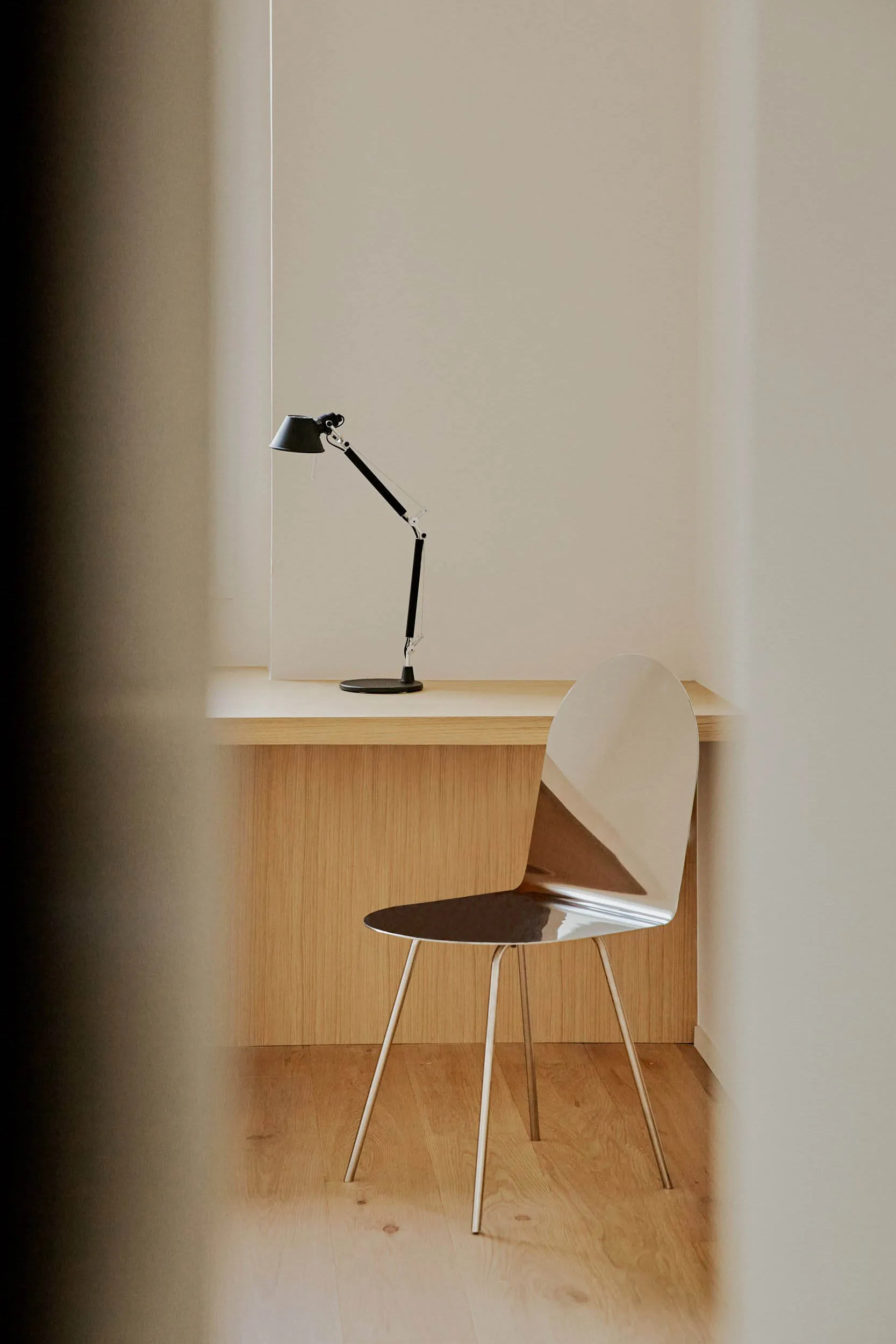 A modern home office featuring a sleek, minimalist desk made of light wood with a black adjustable desk lamp and a modern met