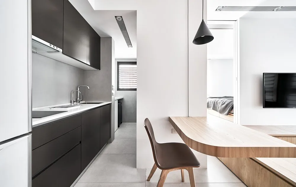 Modern kitchen with black cabinets, white countertops, and wooden table.