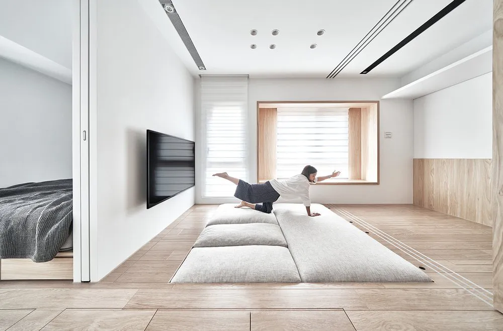 A minimalist living room with a low couch, wooden floor, and large windows.