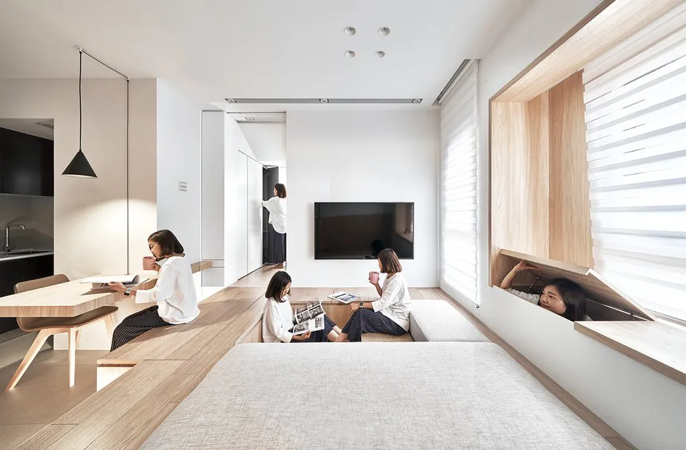 Group of women enjoying coffee in a modern minimalist residential setting with wooden furniture and white walls.