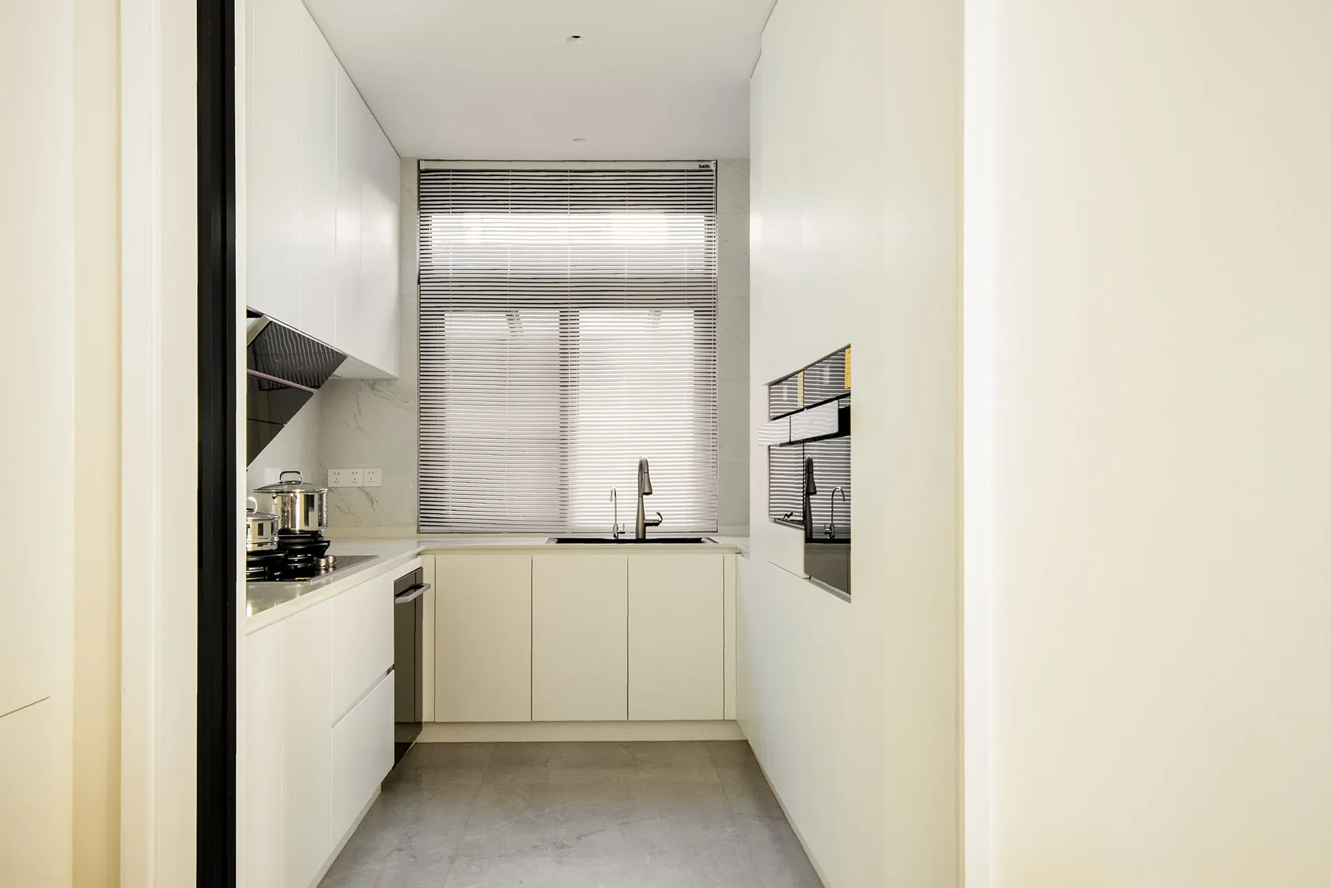 A modern white kitchen with white cabinets, a white countertop, and a large window.