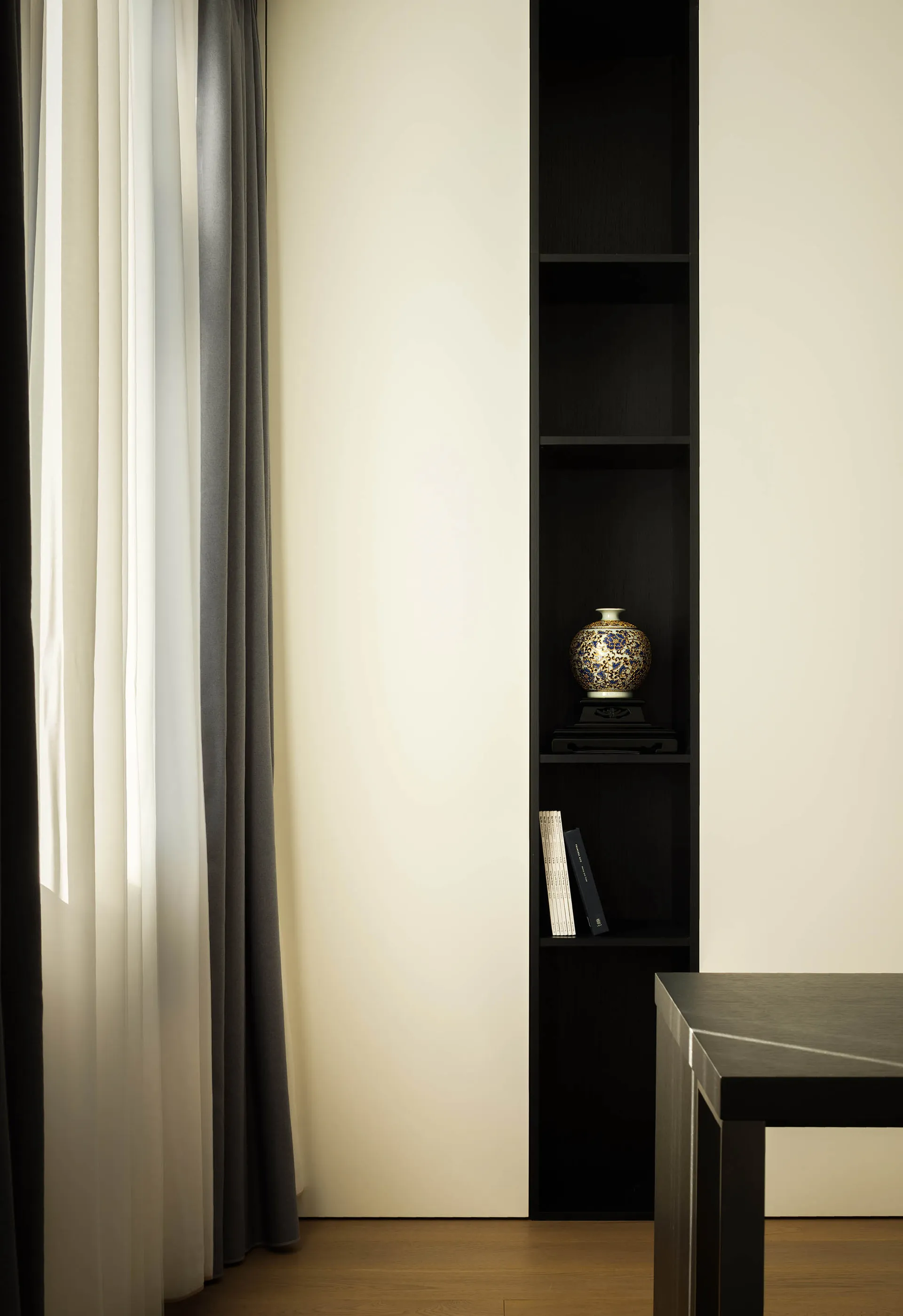A minimalist home office setting with black bookshelf, wooden floor, and modern design.