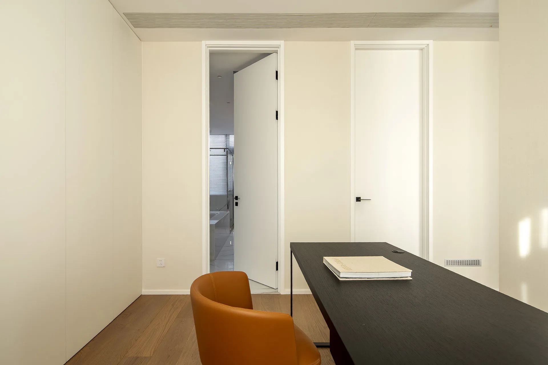 A modern office space featuring minimalist design with white walls, wooden desk, and leather chair.