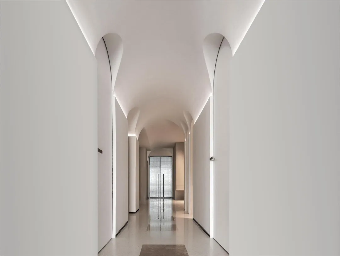 A minimalist white corridor with curved white walls and a glossy floor, featuring recessed lighting and a view to the end of 