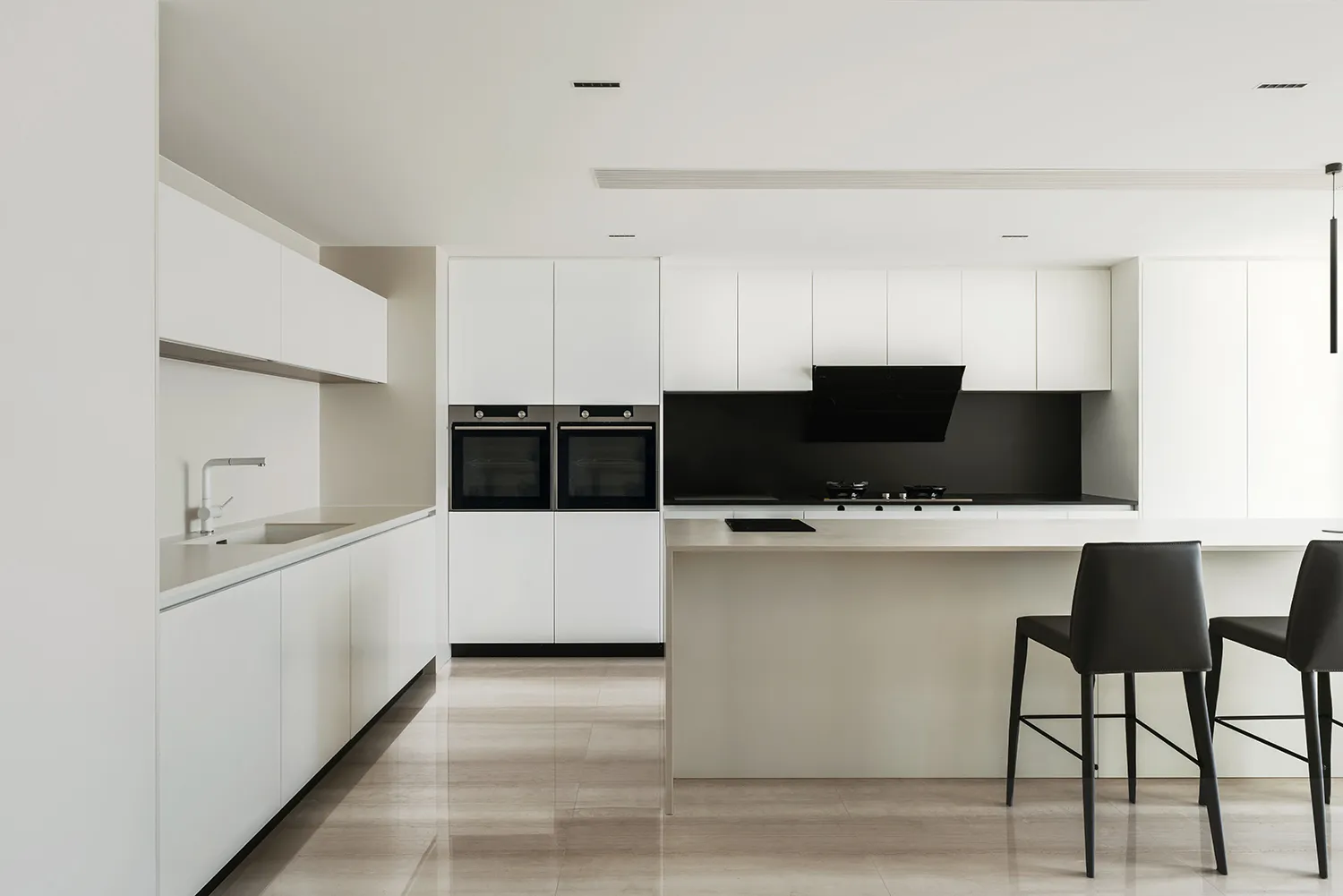 Modern minimalist kitchen with white cabinets, light-colored countertops, and a black backsplash.