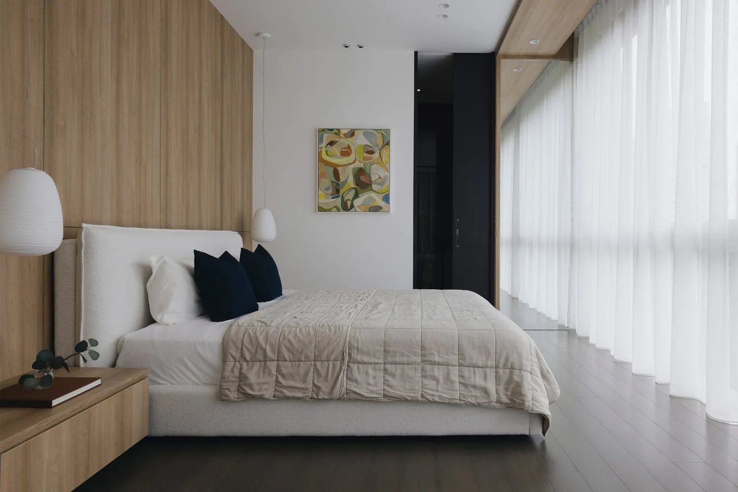 A modern bedroom with a wooden headboard, white bedding, and abstract art on the wall.
