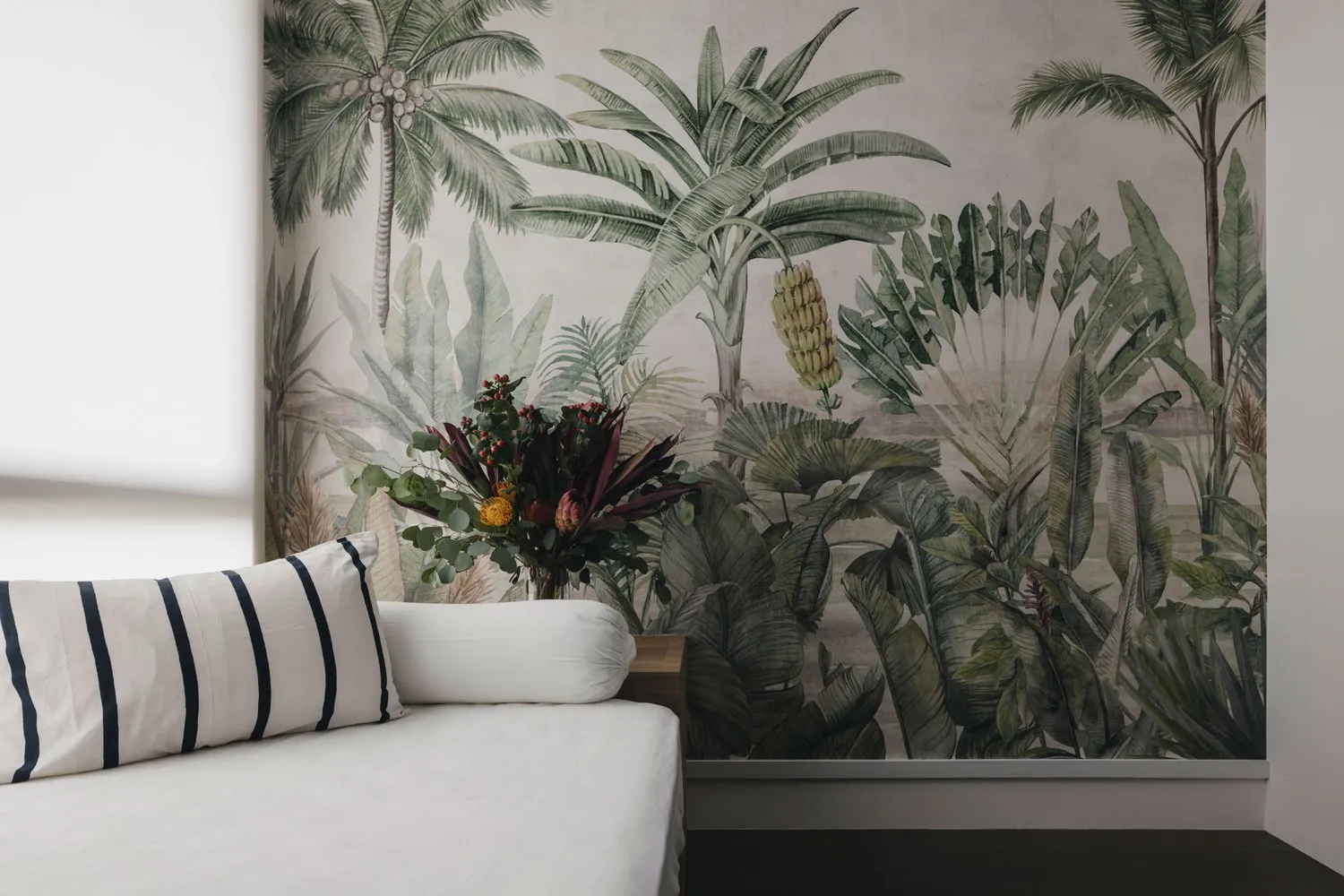 A cozy living space with a white sofa, striped pillows, and a floral arrangement in front of a botanical-themed wallpaper wal
