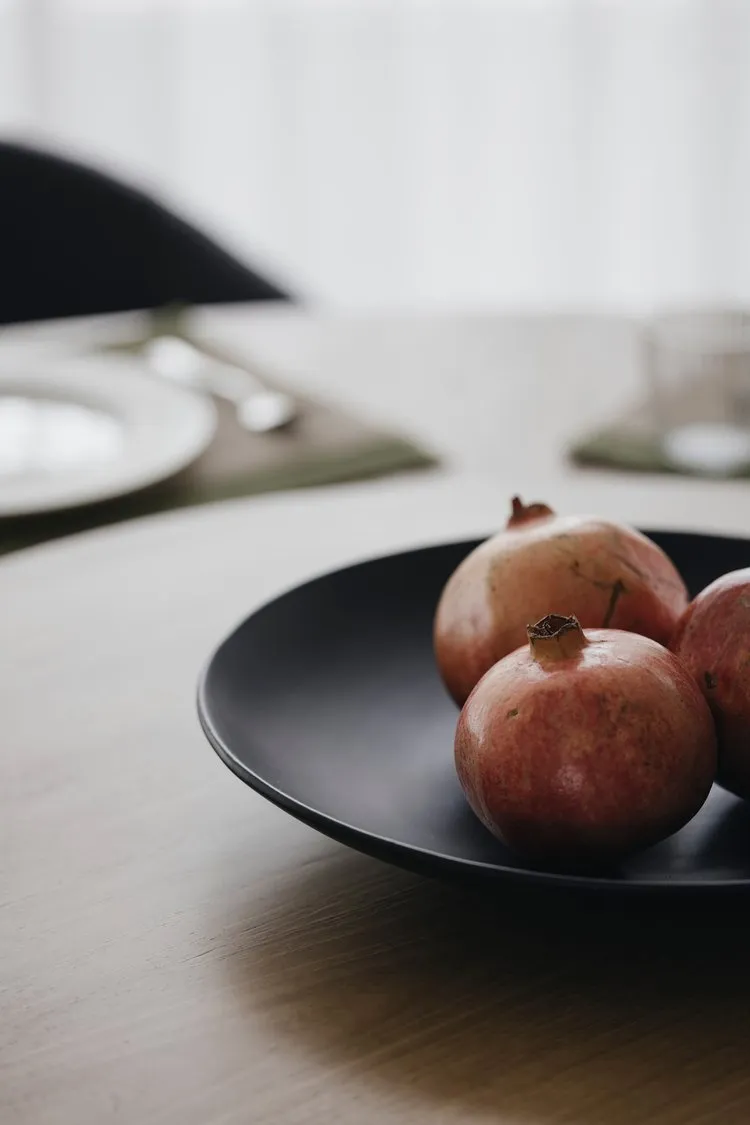 A modern interior design ceramic fruit bowl featuring a bowl filled with organic apples placed on a wooden countertop.