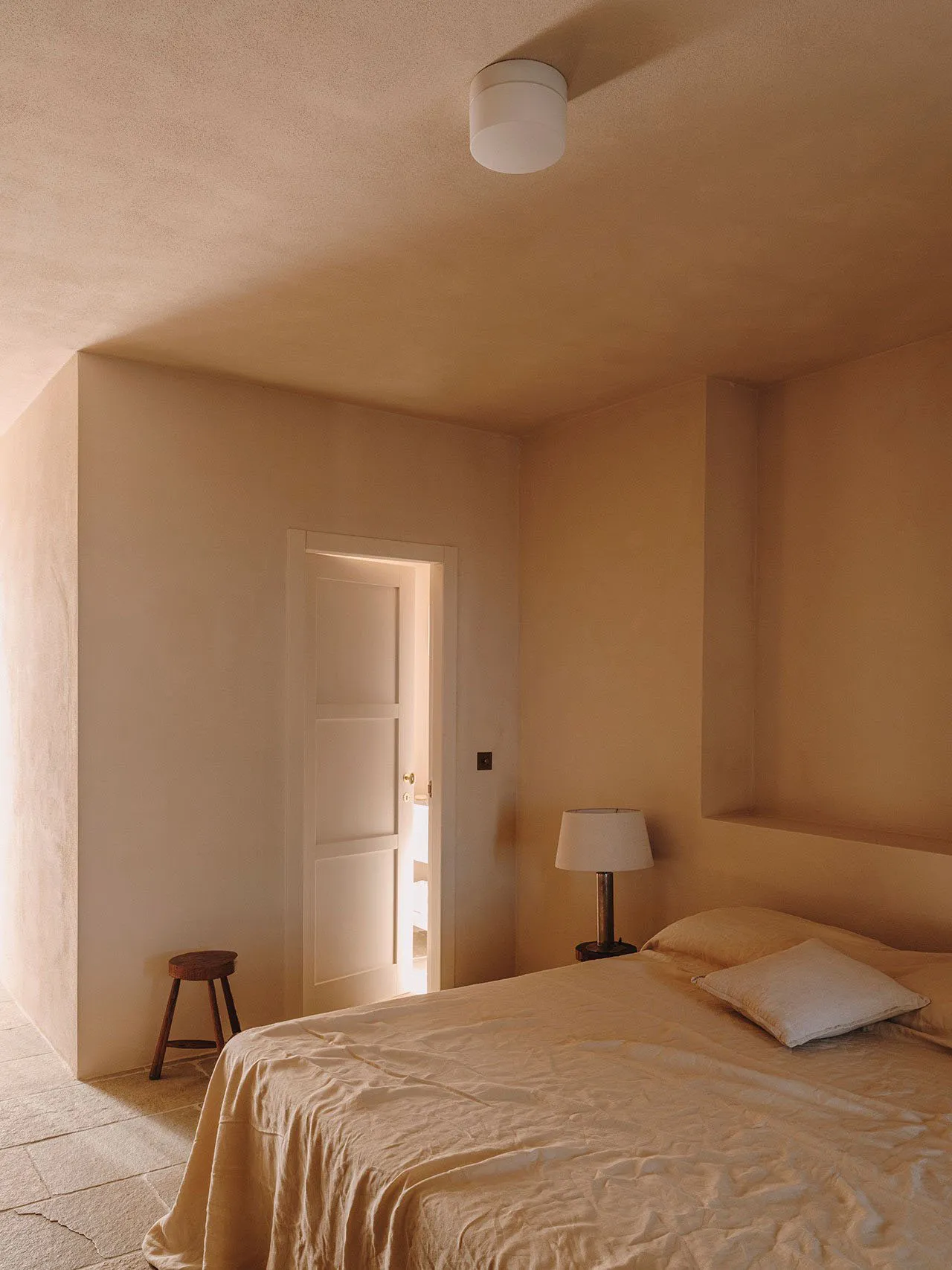 A minimalist bedroom with beige plaster walls and a simple bed setup.