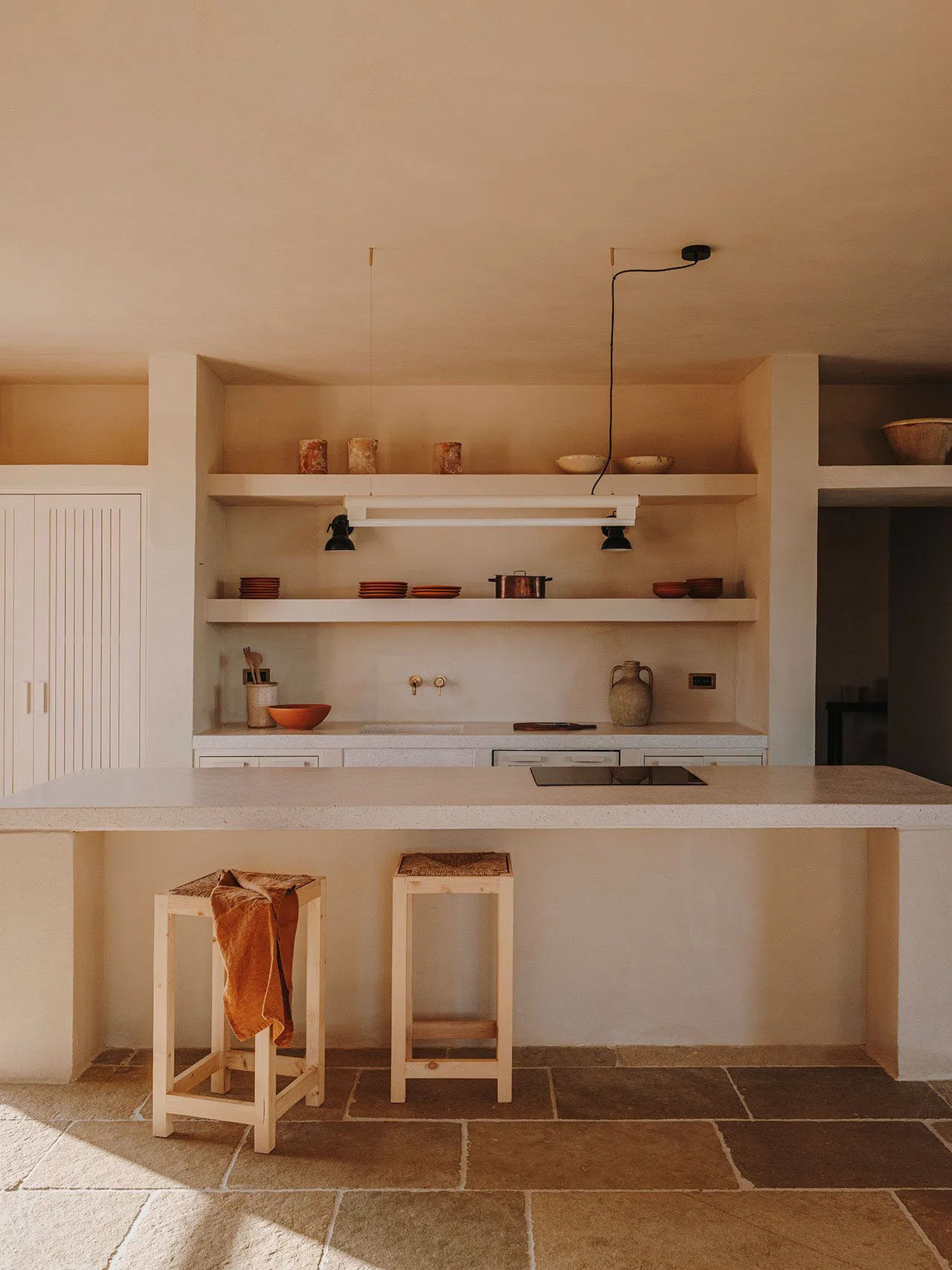 A minimalist residential kitchen featuring concrete counter tops, shelves, and stools.
