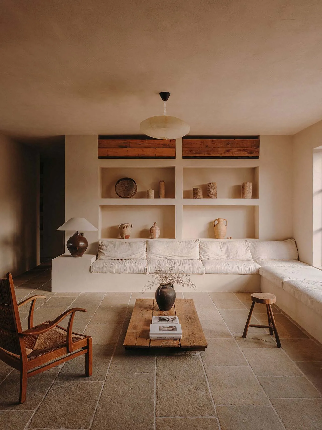 A minimalist living room with a concrete floor, wood furniture, and built-in shelves.