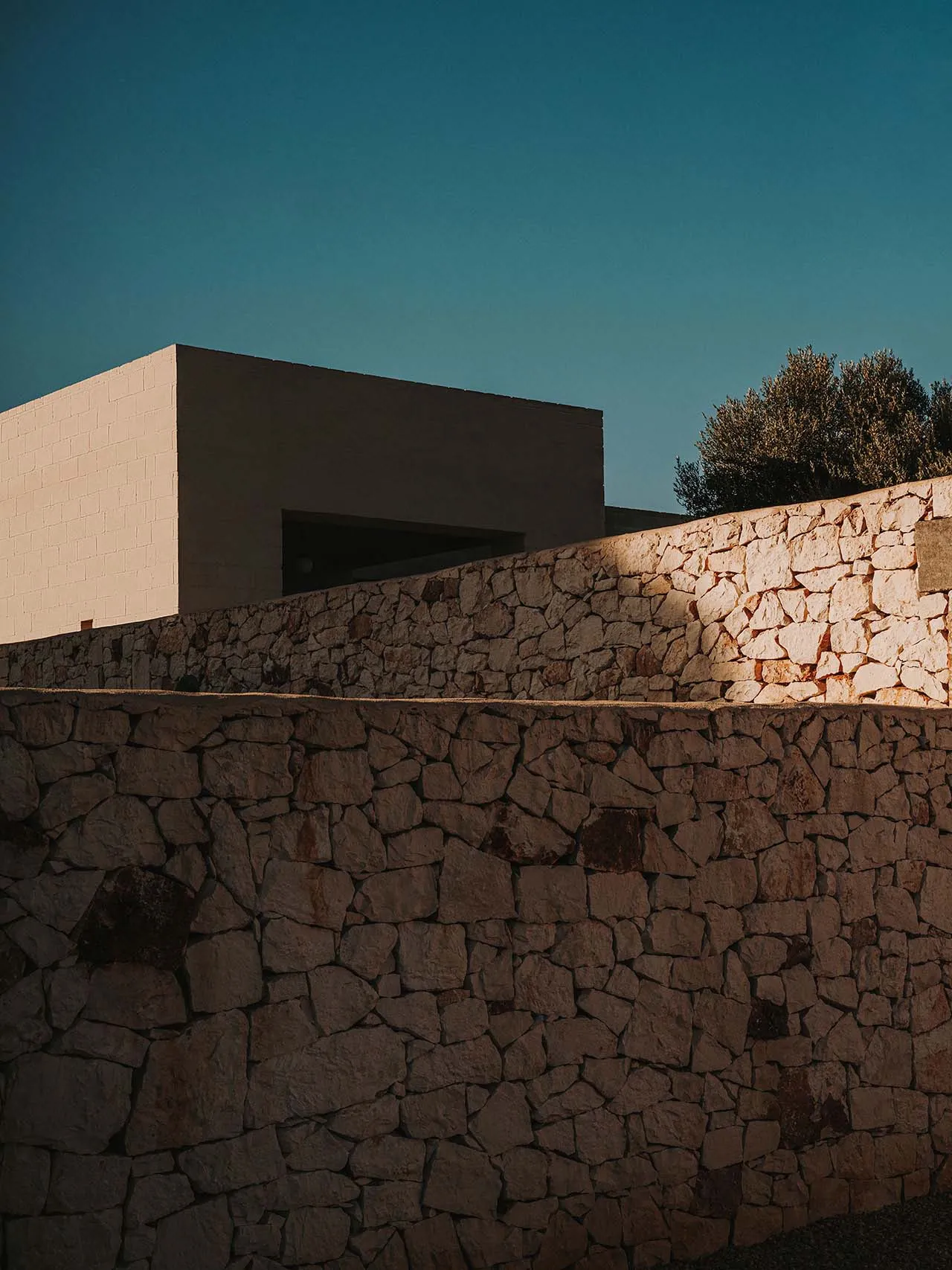 A modern building featuring a stone wall during sunset.