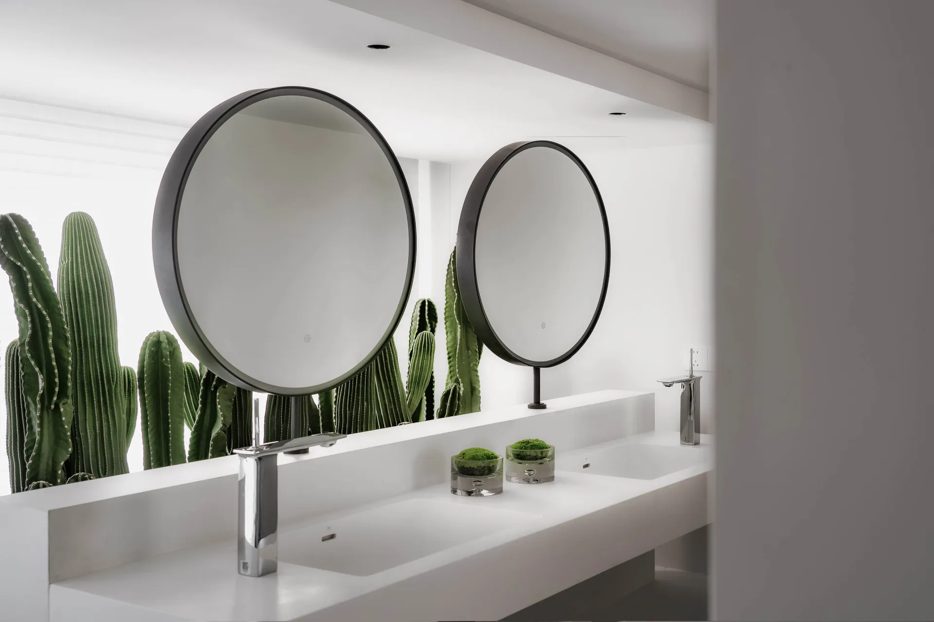 Modern minimalist bathroom with concrete countertop, white sinks, chrome faucets, and round mirrors.