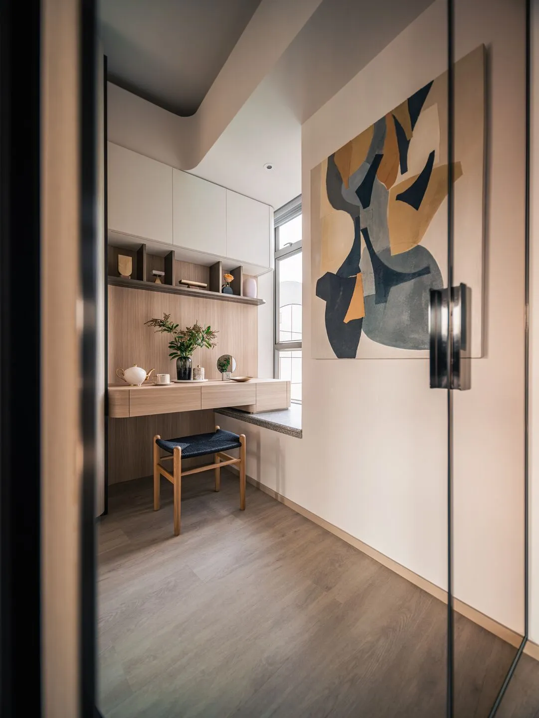 A modern home office with light wood furniture, marble accents, and glass elements.