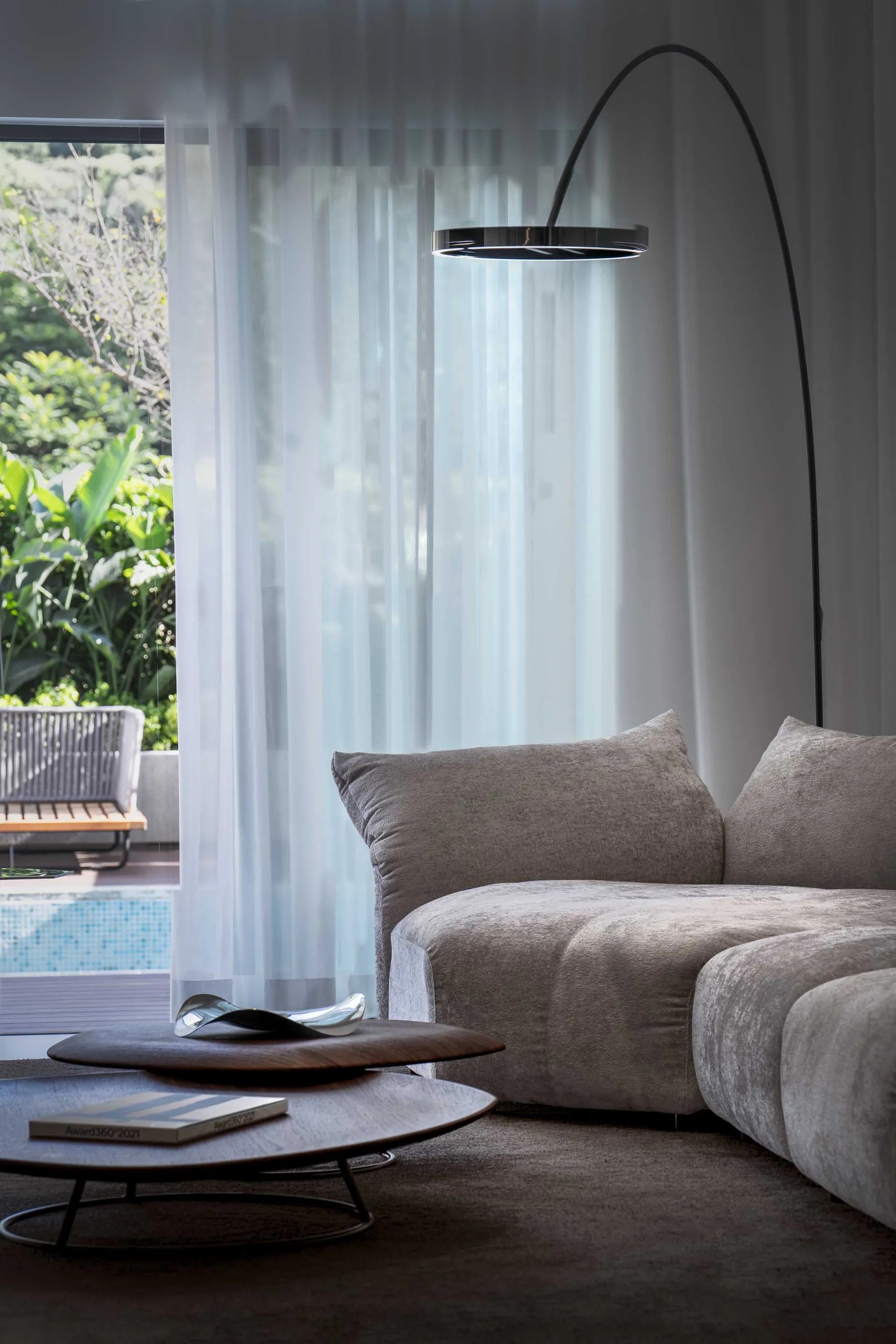 Modern minimalist living room featuring a fabric sofa, glass lamp, and sheer curtains.