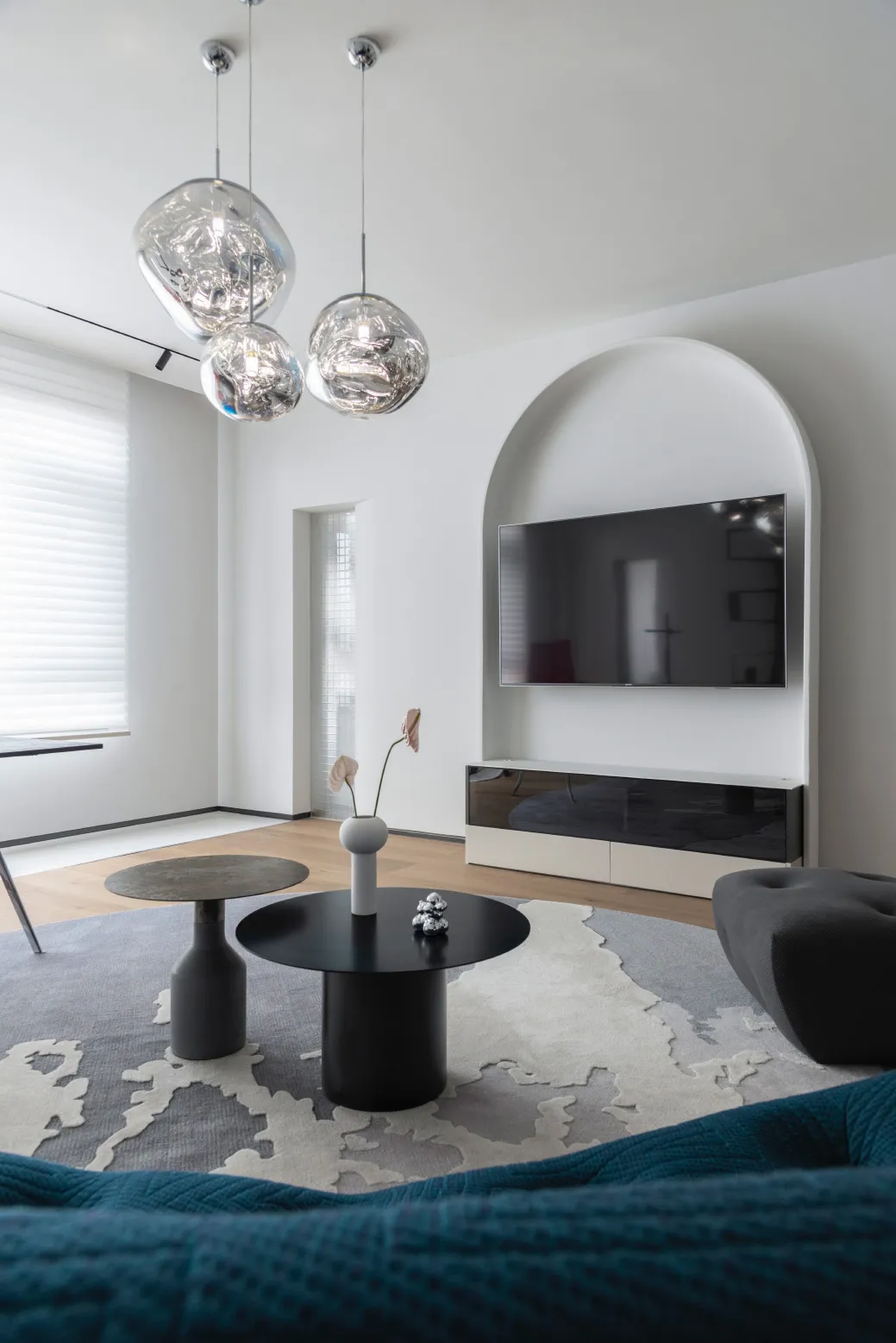 A modern minimalist living room featuring metal pendant lights, wooden flooring, and fabric seating.