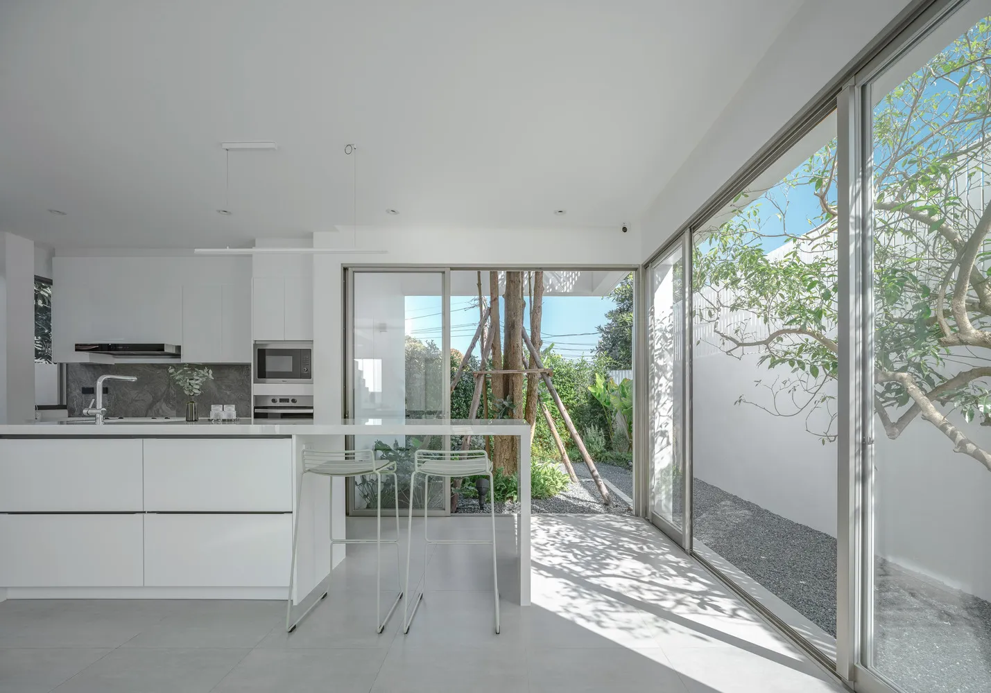 Modern, minimalist residential kitchen with large glass windows and a white color palette.