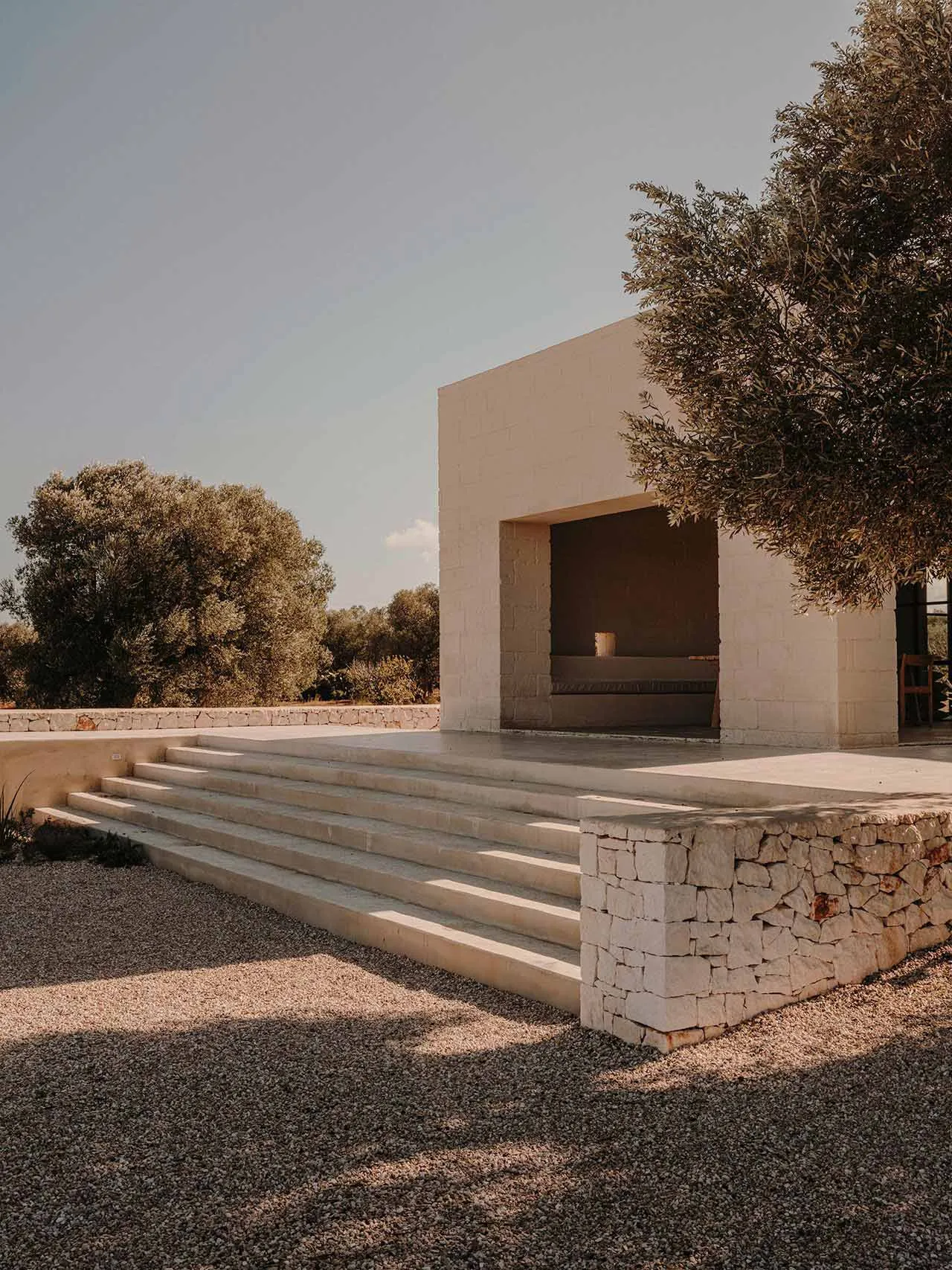 A modern architectural space with a concrete exterior, featuring a central open area surrounded by a stone wall and steps lea