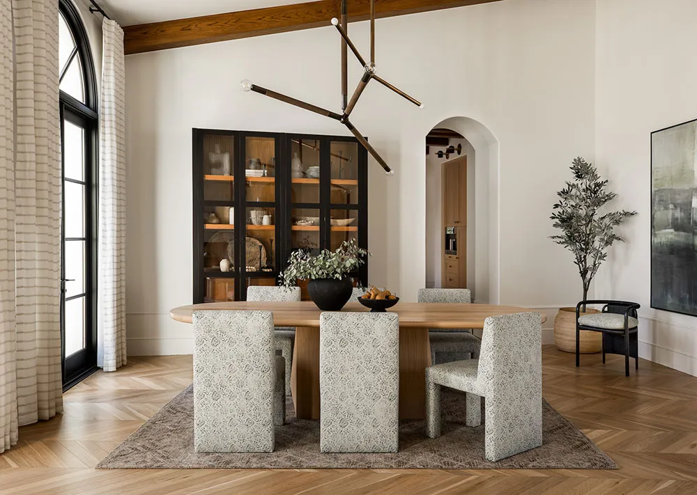 A modern dining room featuring a wooden table, patterned chairs, and a glass-fronted cabinet.