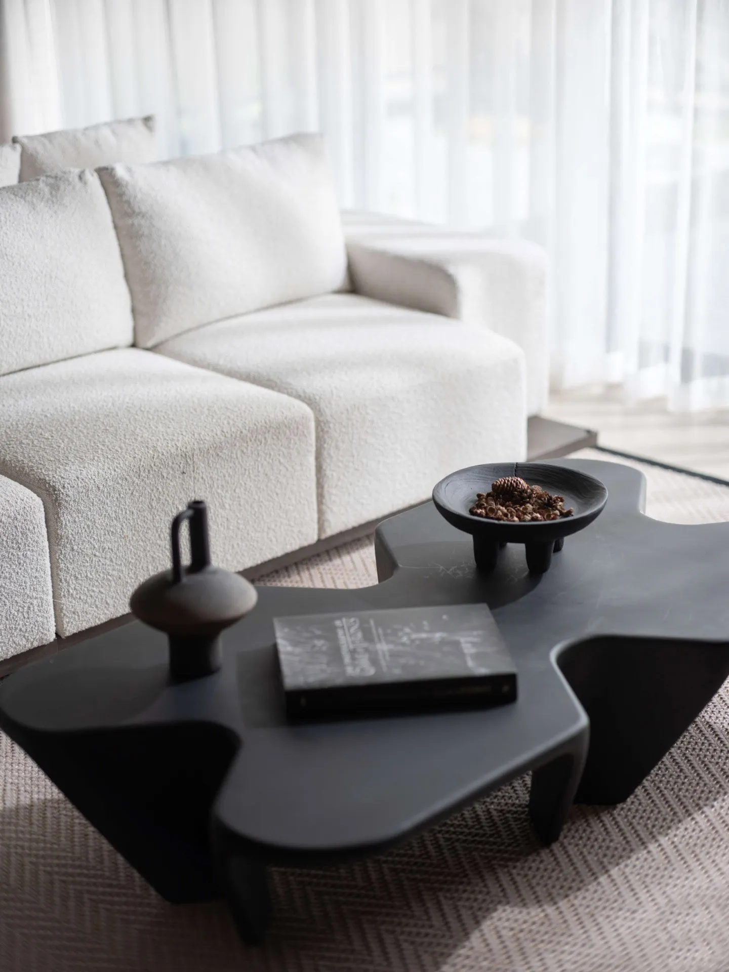 A modern living room with a white textured fabric sofa and a uniquely shaped black coffee table.