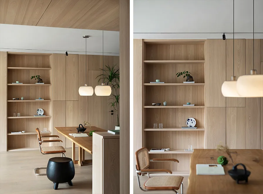 A minimalist office space featuring wooden walls and shelves with books and decorative items, illuminated by hanging lamps.