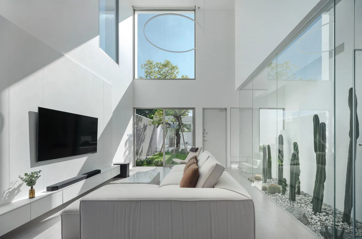 A minimalist living room features a white sofa, modern design, large windows, and a glass wall.