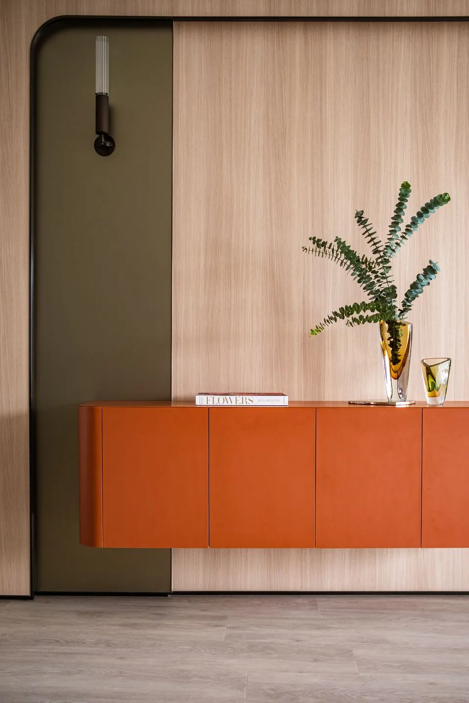 A modern living room featuring a wooden cabinet with orange doors and a vase with green leaves, set against a wooden wall and
