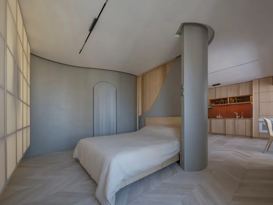 A modern bedroom with light wooden flooring and a bed with a white cover.