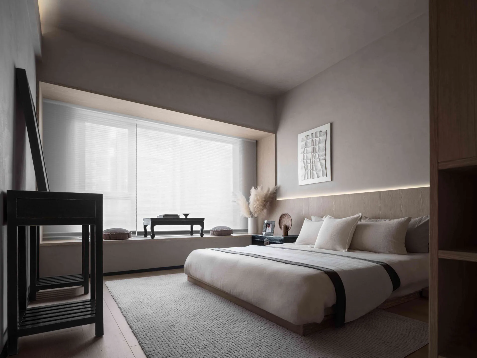 A minimalist bedroom with neutral tones, featuring a bed, nightstand, and artwork above the bed.