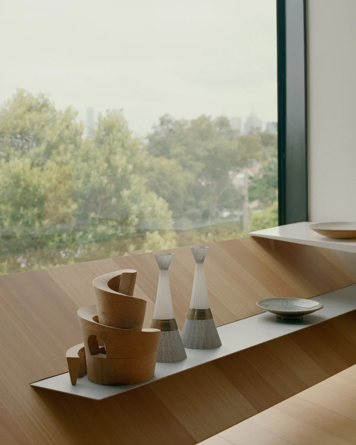 A minimalist table setting featuring wooden and ceramic elements against a large window.