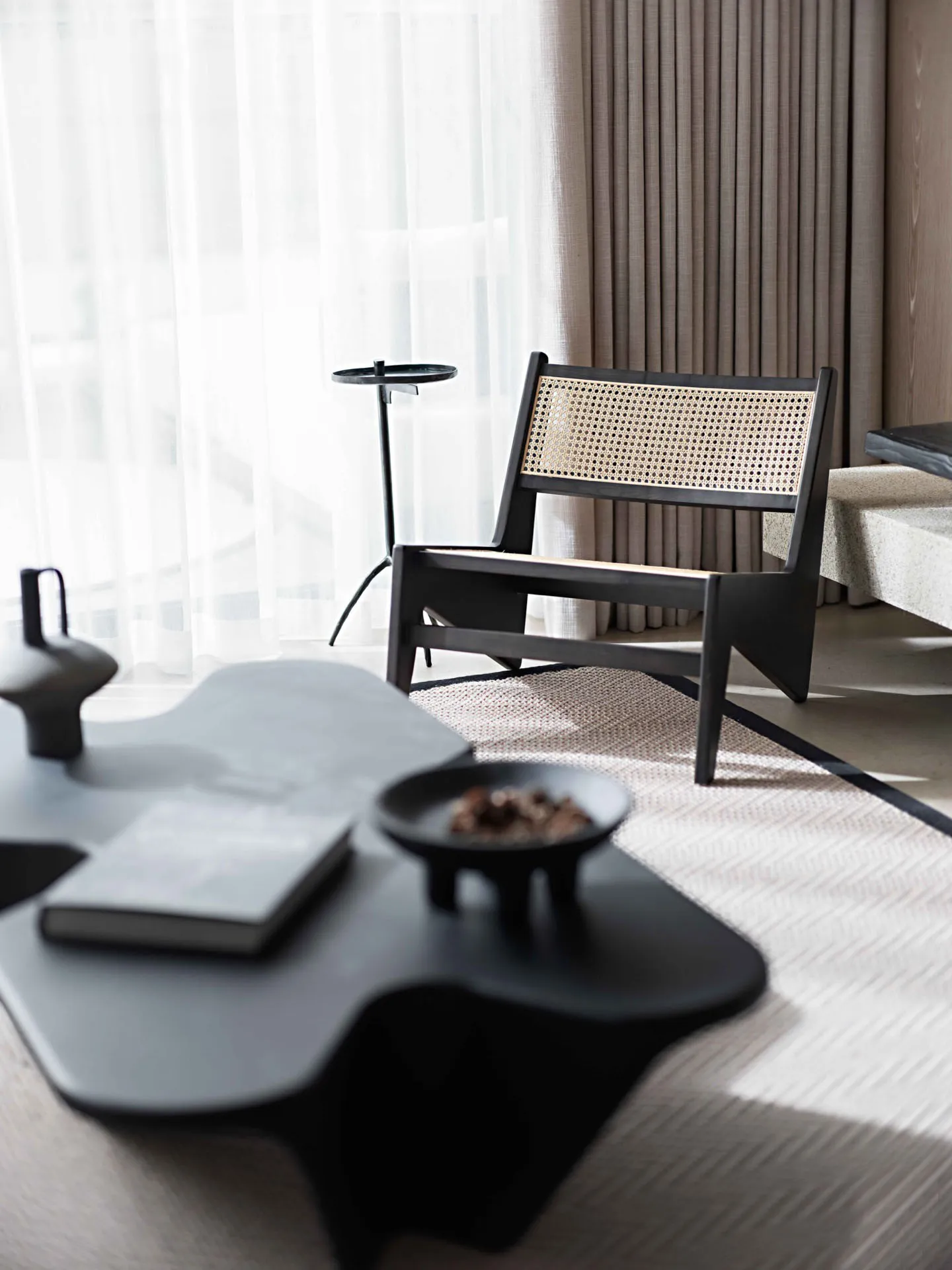 A modern living room featuring a black coffee table with sculptural legs and a black modern lounge chair with bamboo backrest
