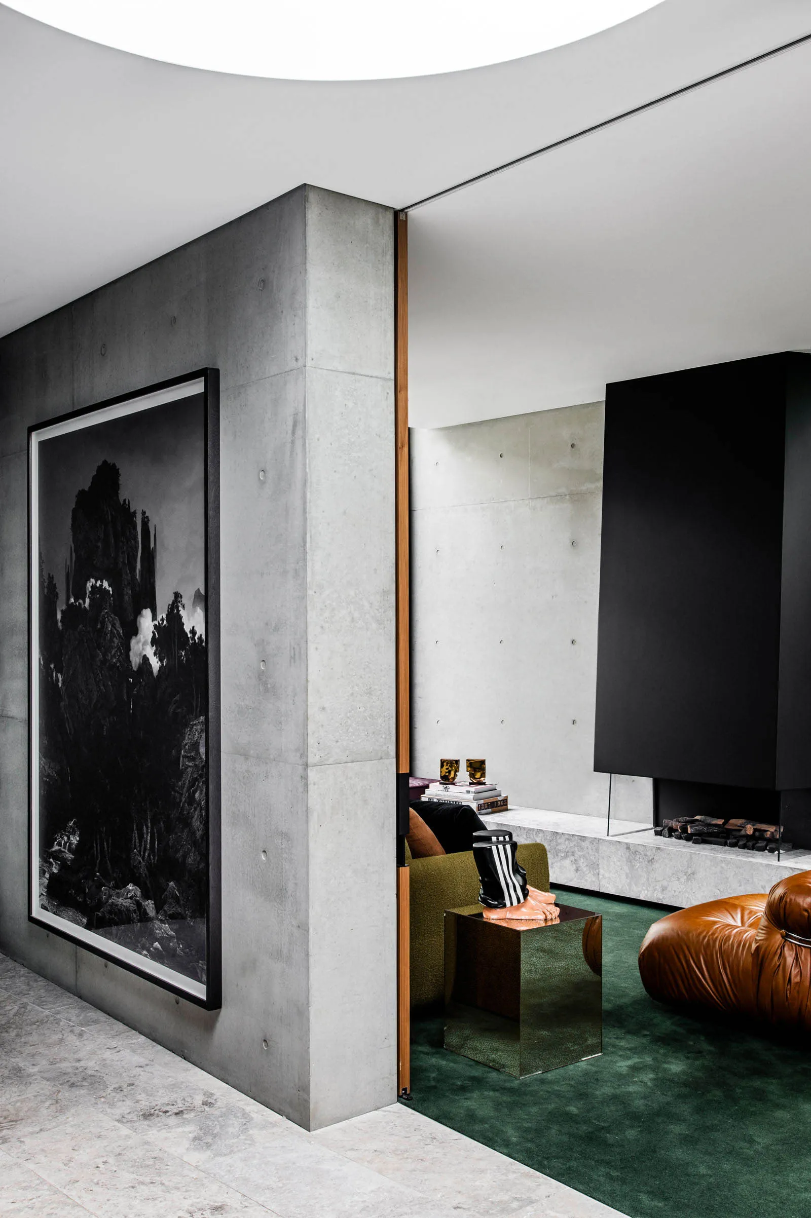 A modern living room featuring a concrete wall with a large black and white photographic print, a green carpet, and a brown l