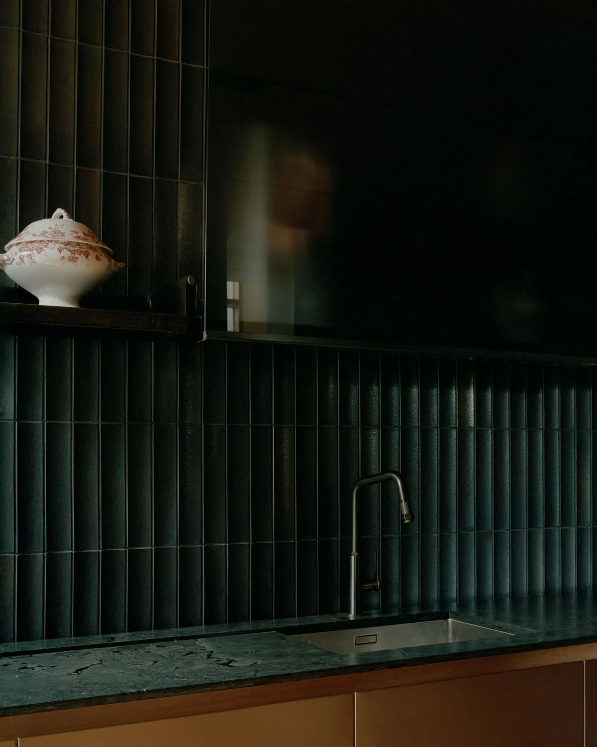 A well-equipped kitchen with marble countertops and a sink, featuring sleek black tiles and a decorative ceramic dish.