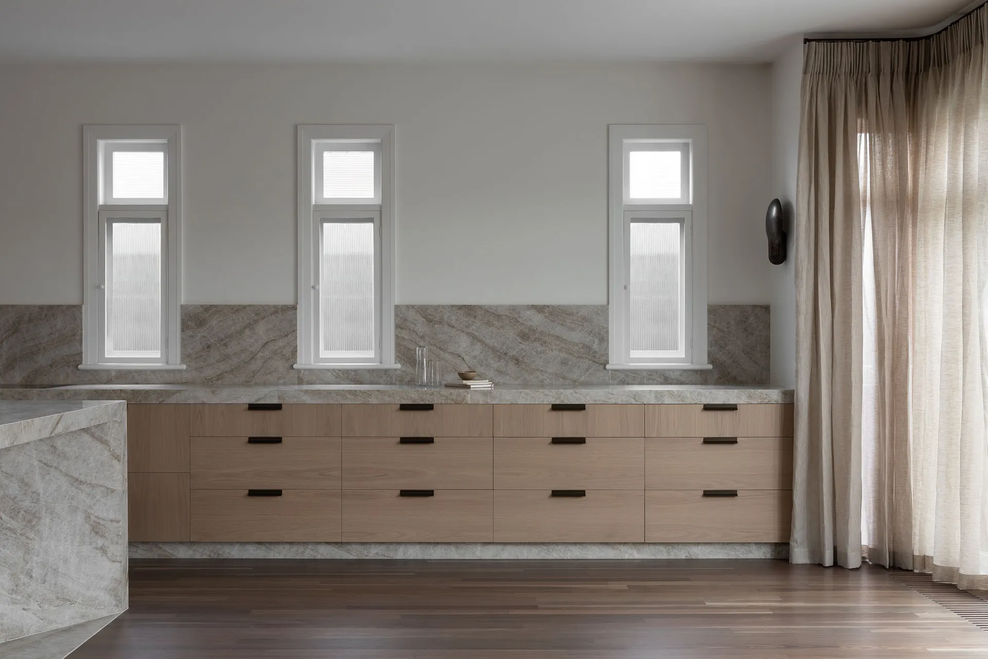 Modern minimalist kitchen with natural wood cabinets and marble countertop.