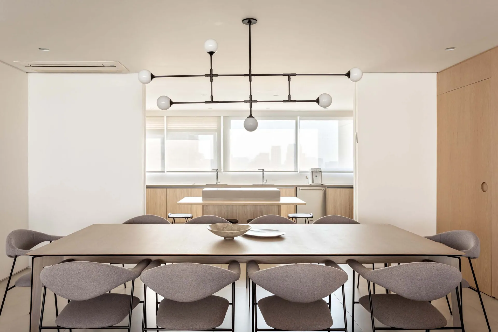 A modern minimalist kitchen space featuring a wooden dining table, concrete kitchen island, and glass pendant lights.