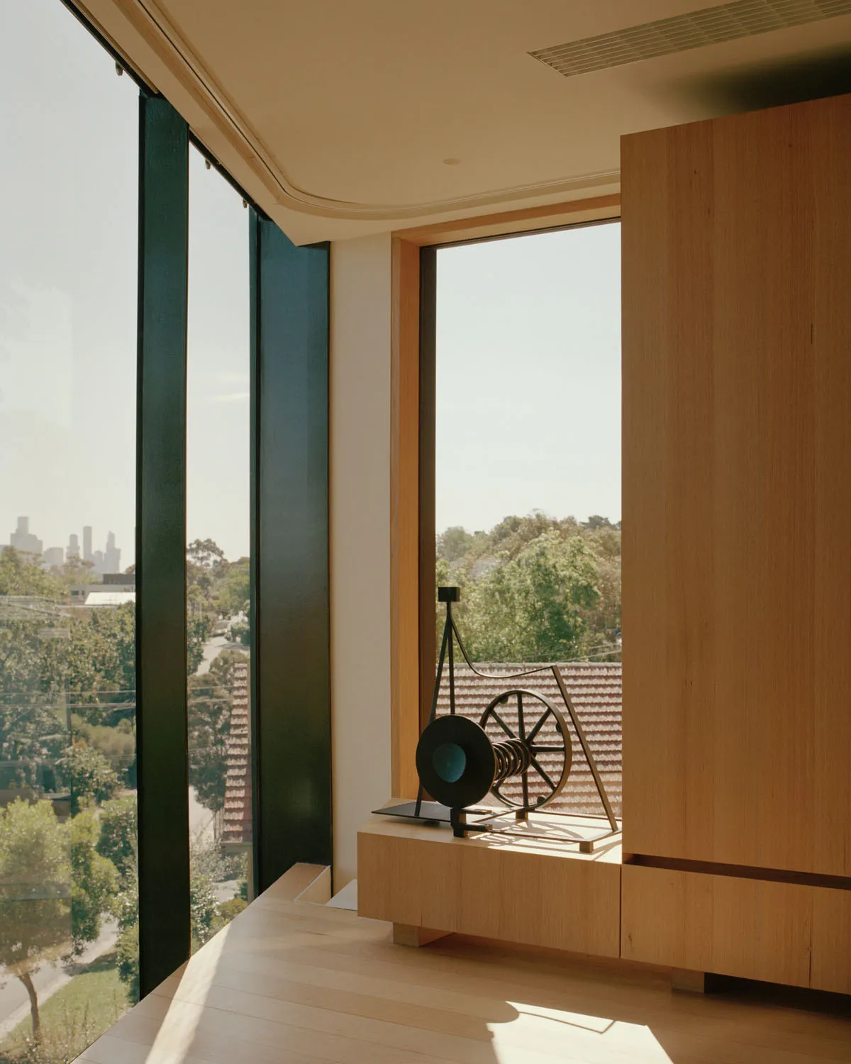 Industrial interior space featuring a metallic wheel sculpture on a wooden shelf with large windows overlooking a cityscape.