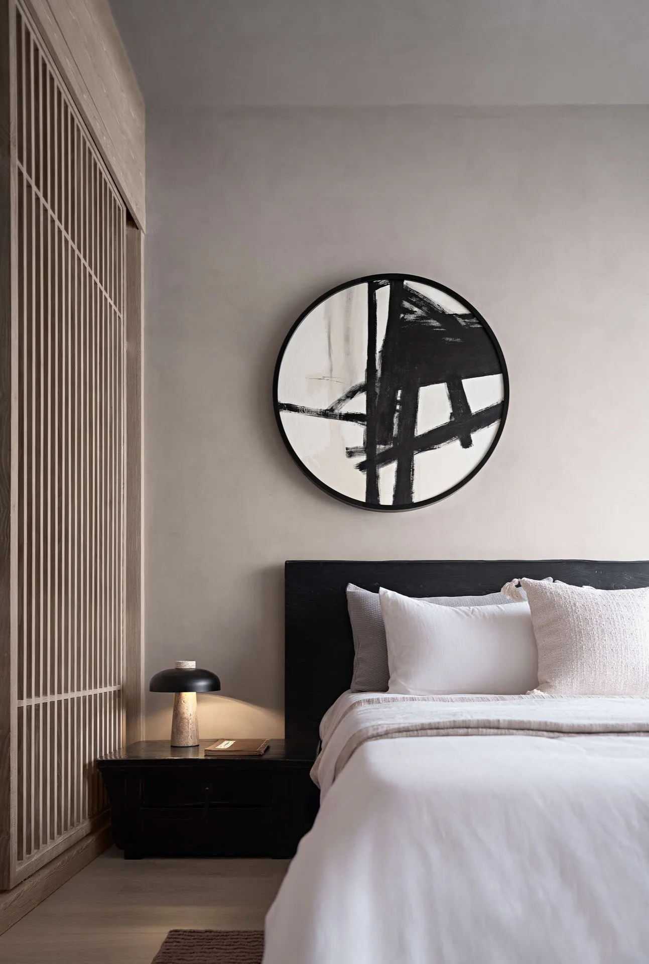 A minimalist bedroom with a black-framed bed, white bedding, neutral-toned wall paint, and a black side table lamp.