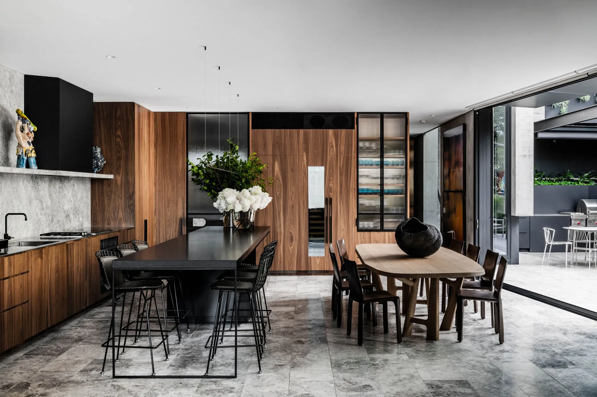 Modern kitchen dining room featuring wooden and concrete finishes with a long black table and white bar stools.