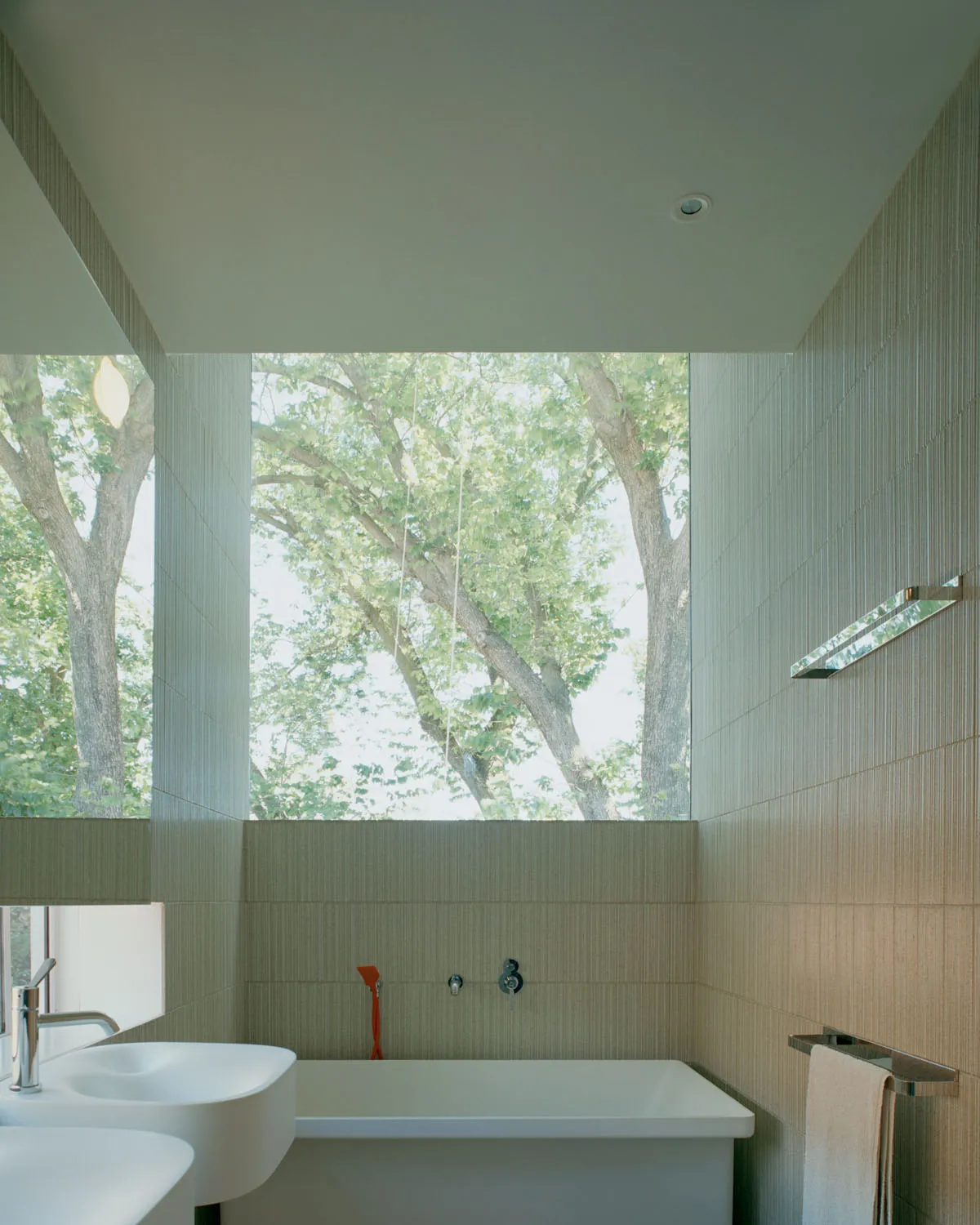 Modern minimalist bathroom featuring a white bathtub, sink, and towel rack with a window showing trees outside, all set again