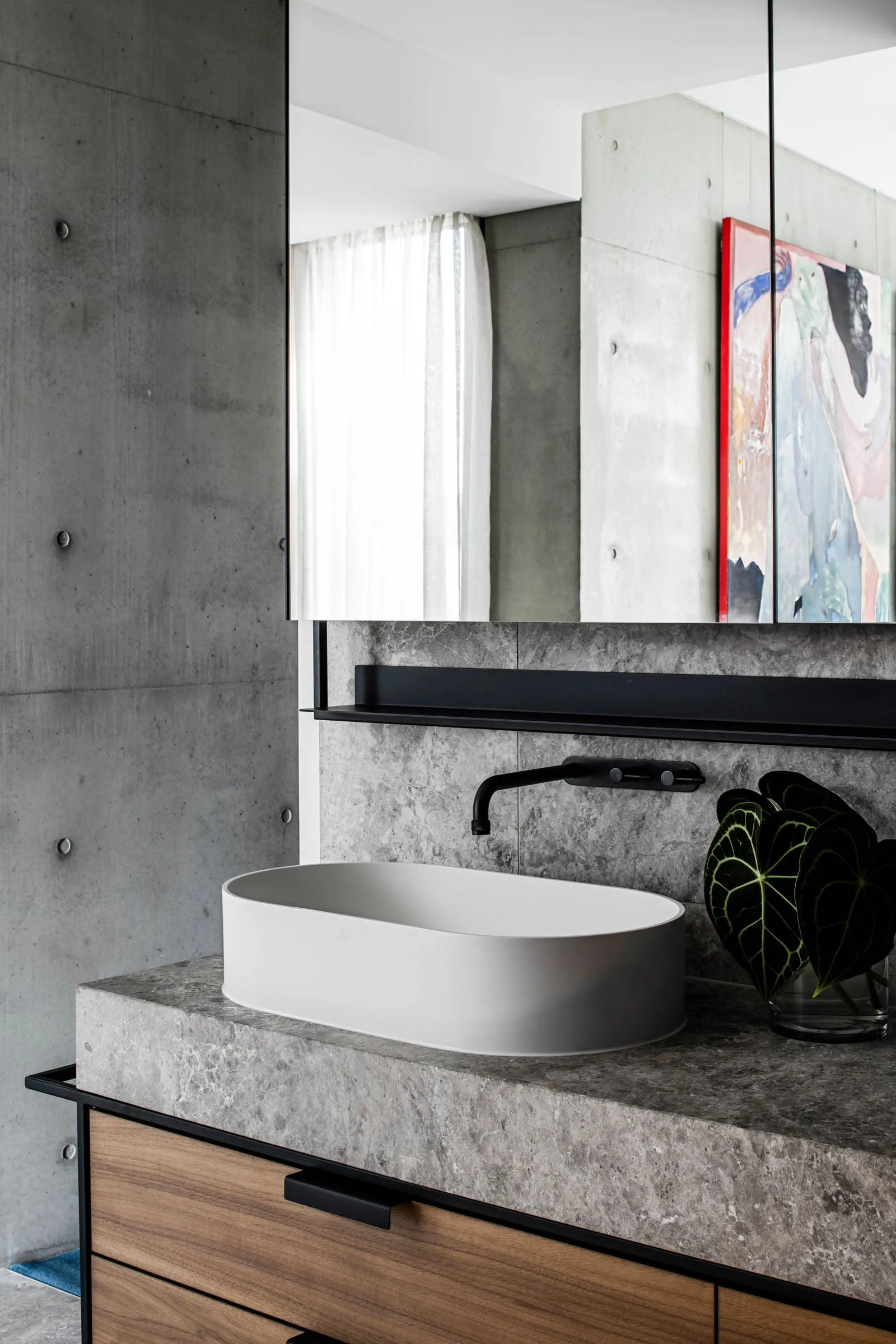 A modern bathroom with a white countertop and sink, featuring a black faucet and a plant in a glass vase.