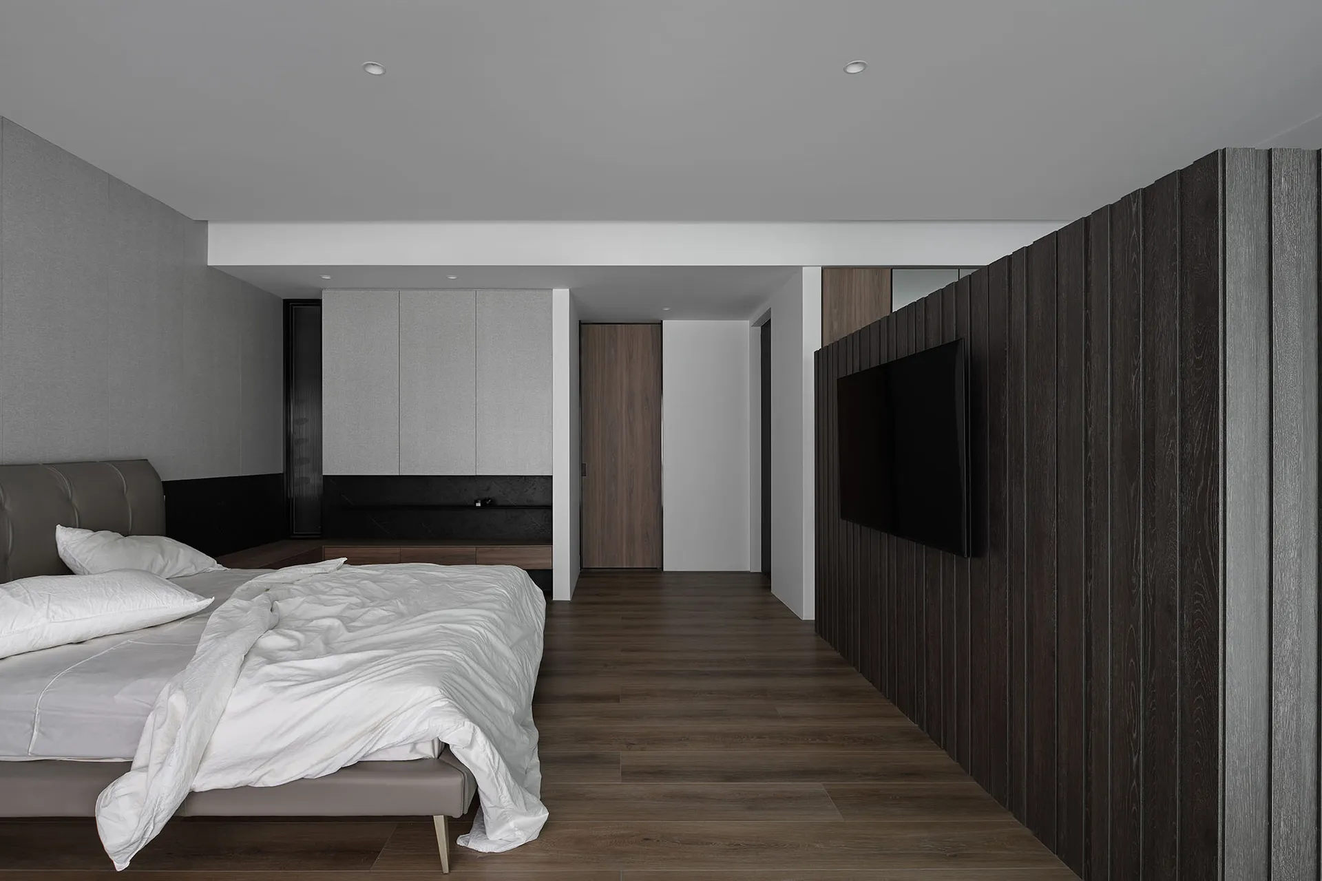 A modern minimalist bedroom with dark wood paneling and a white bedspread.
