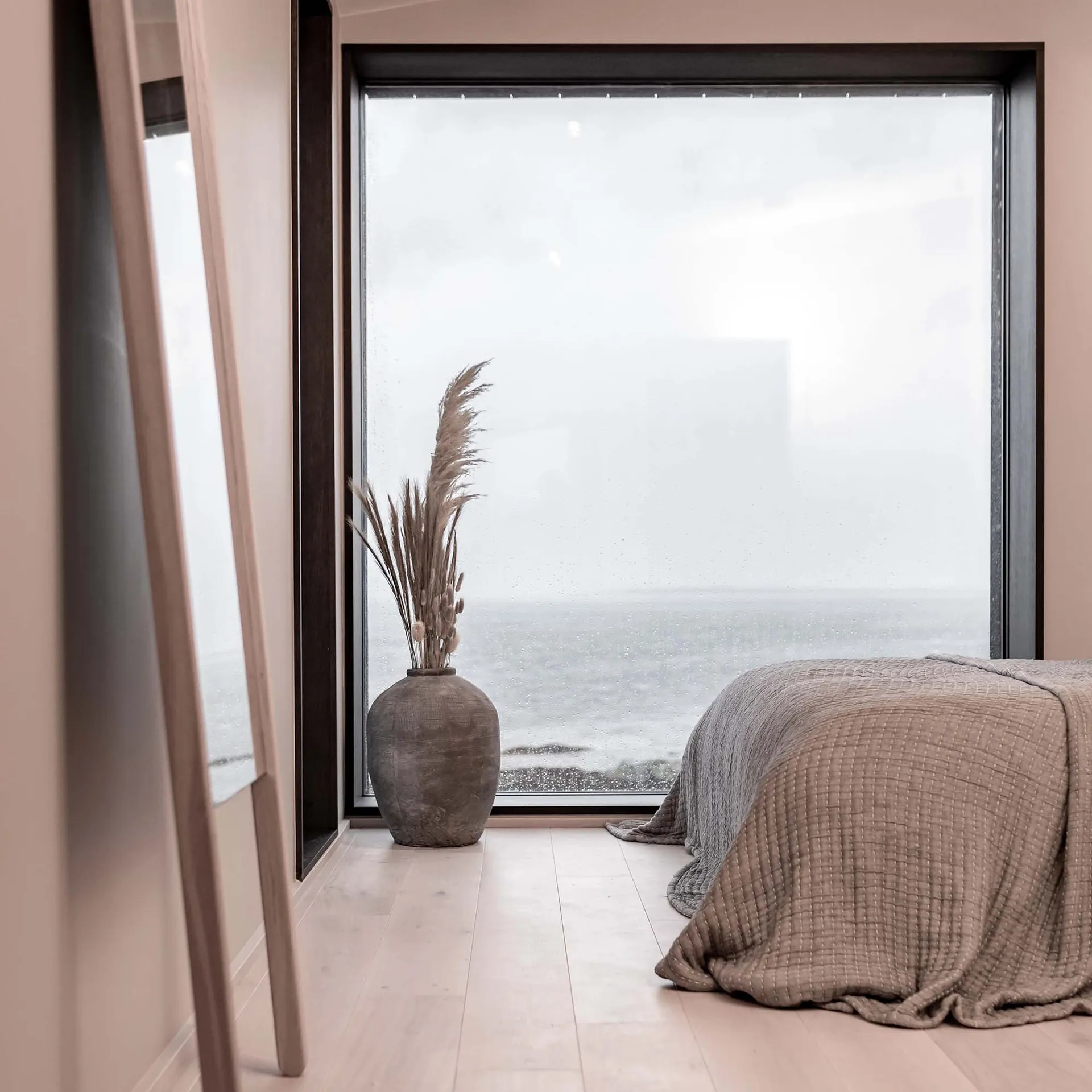 Minimalist bedroom with a wooden floor, a fabric-covered bed, and a decorative vase
